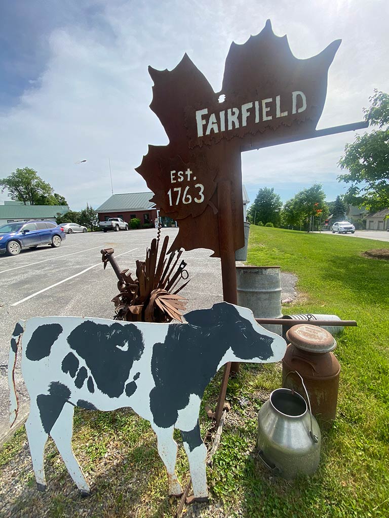A photograph of the Fairfield town offices with a maple leaf, spotted cow, and olf milk pails