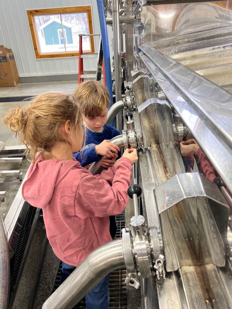 A young boy and girl look at an aluminum holding tank with sap