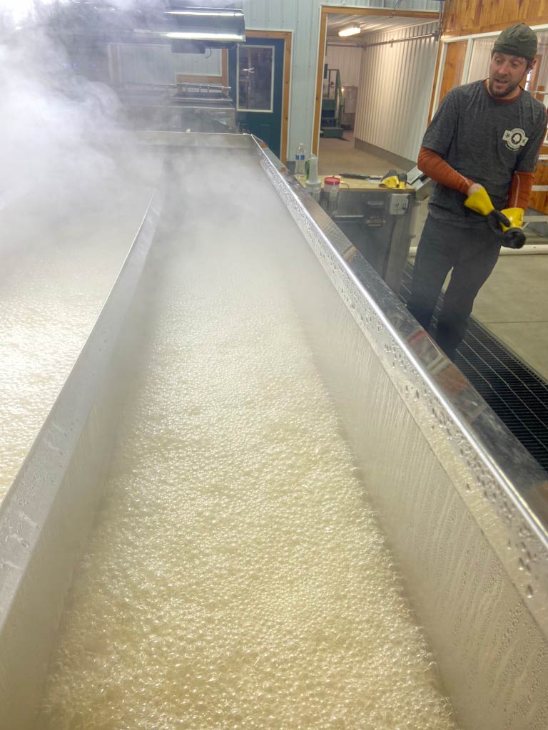 Kyle Branon looks over an evaporator pan of boiling maple syrup