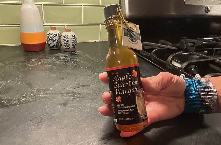 Photo of hand holding a bottle of Branon Maple Bourbon Vinegar in a kitchen